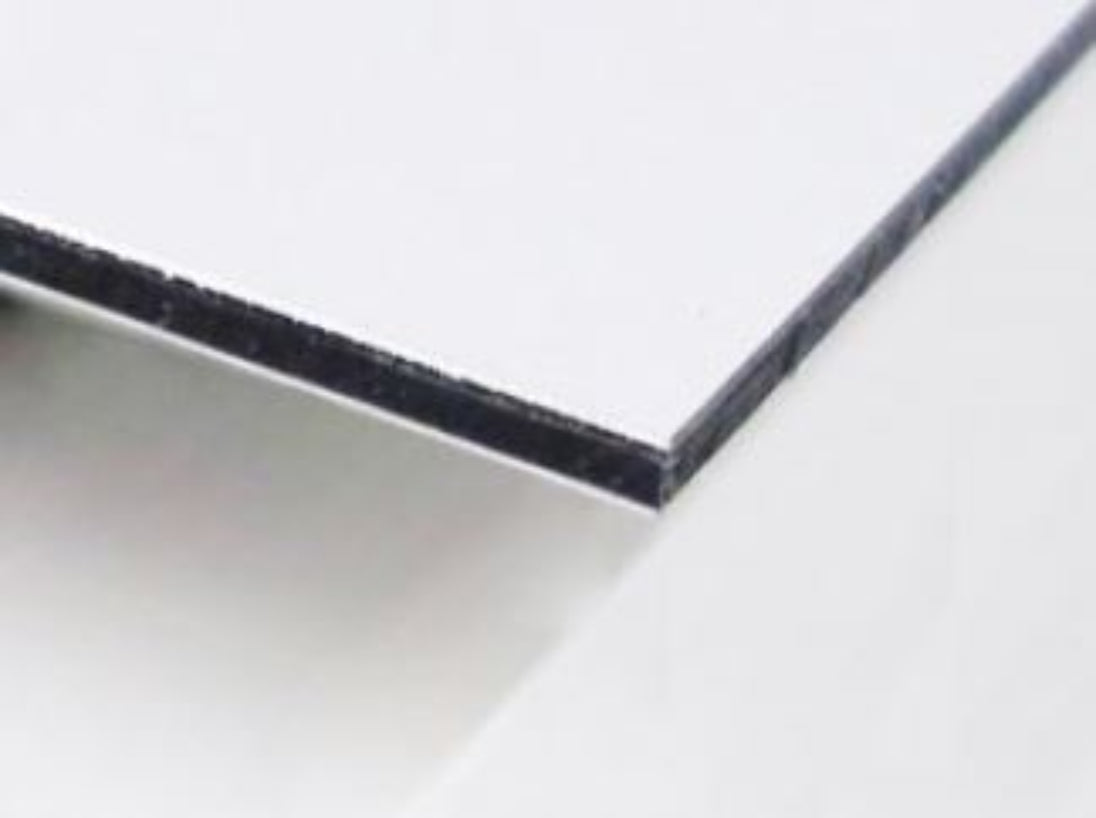 Edge of a white matte aluminum composite panel showing the back adhesive layer.