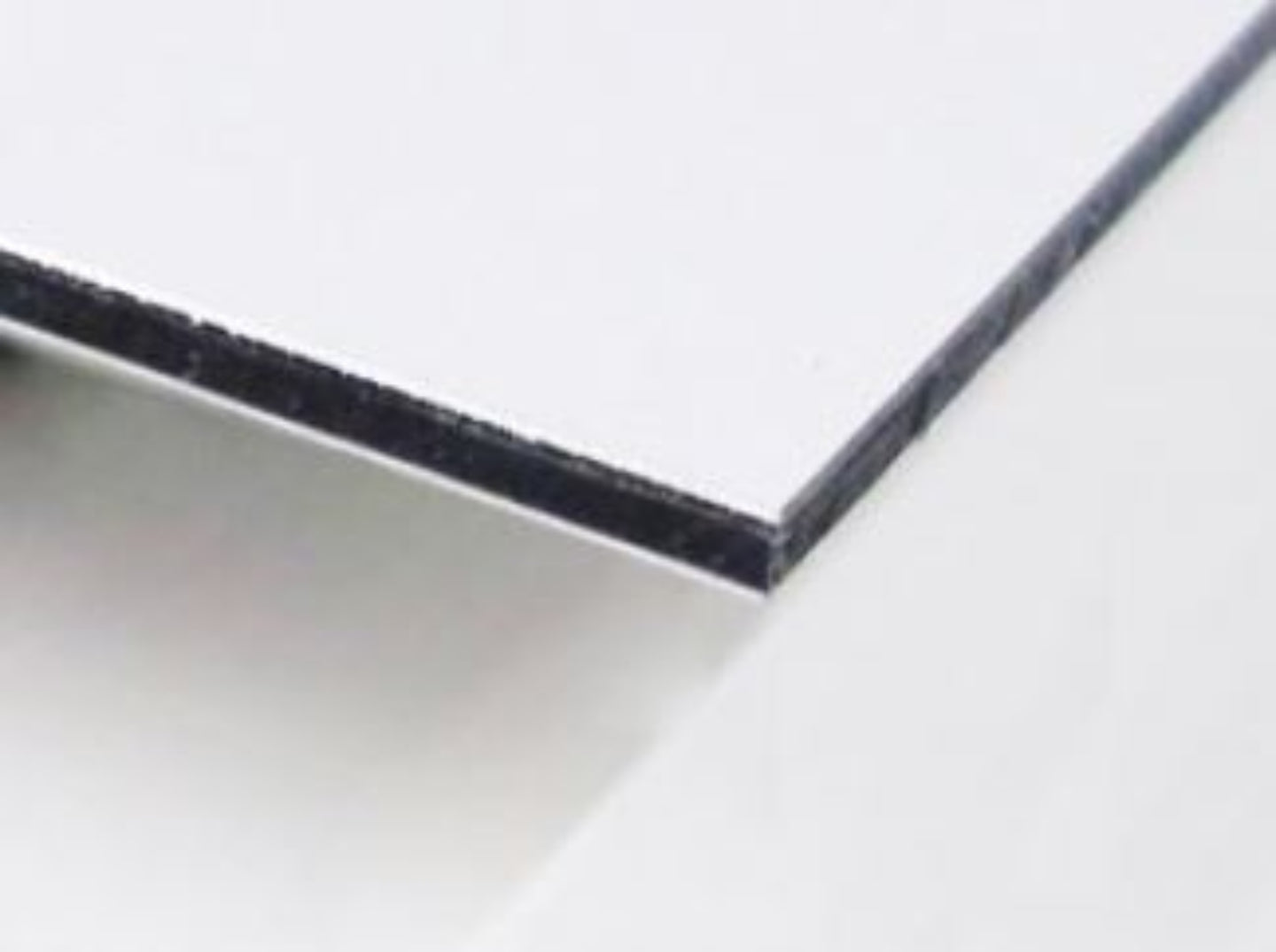 Edge of a white matte aluminum composite panel showing the back adhesive layer.