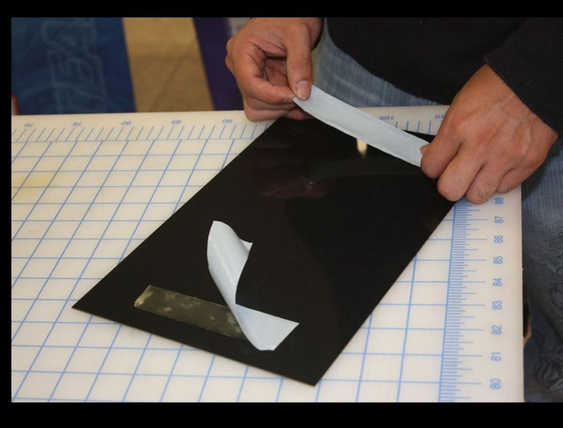 Person measuring a black sheet with a white object on a grid surface