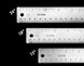 Three metal rulers with measurements in inches and millimeters on a black background