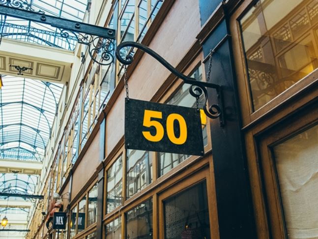Number 50 sign hanging from a building in an indoor shopping arcade.