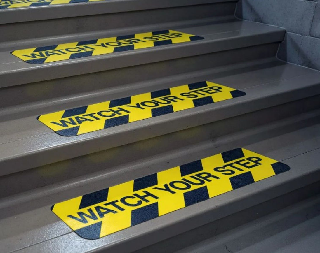 Stair treads with 'Watch Your Step' warning labels on a set of stairs.