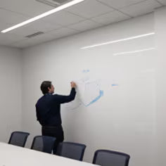 Person using a whiteboard in a conference room with chairs and lights.