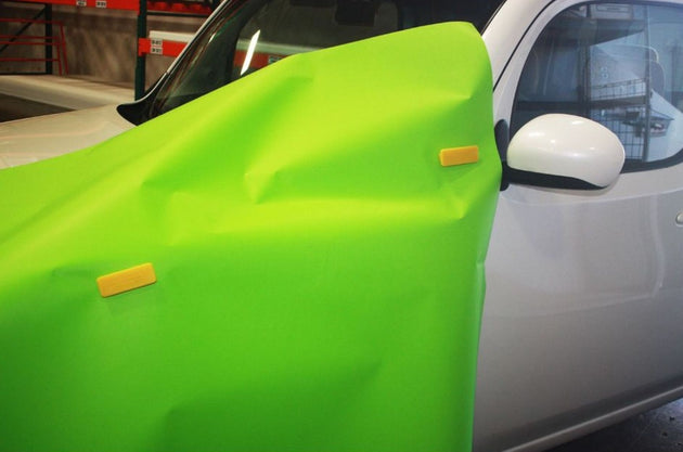 Car with a green cover and yellow stickers in a garage setting