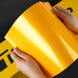 Person holding a roll of yellow vinyl wrap against a black background
